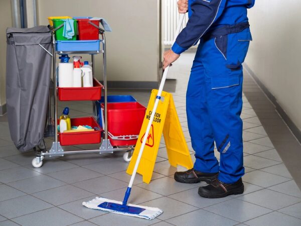 A man in blue overalls mopping the floor.