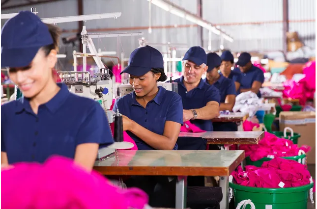 A group of people in blue shirts and hats working on pink bags.