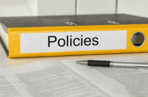 A yellow binder labeled 'Policies' with a pen on documents.