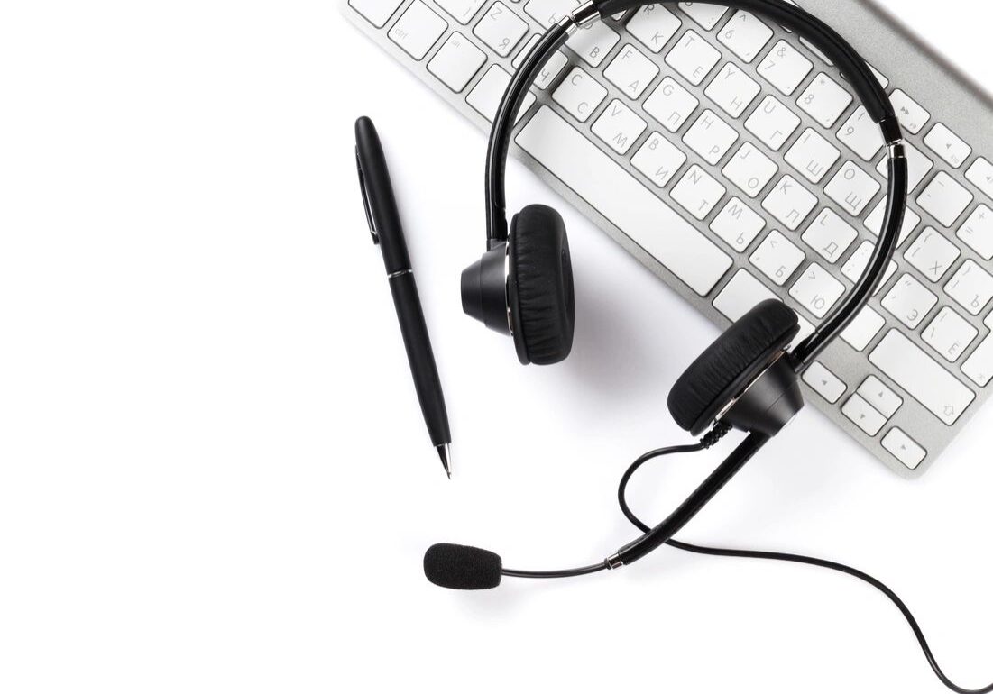 A keyboard, headphones and pen on top of the table.